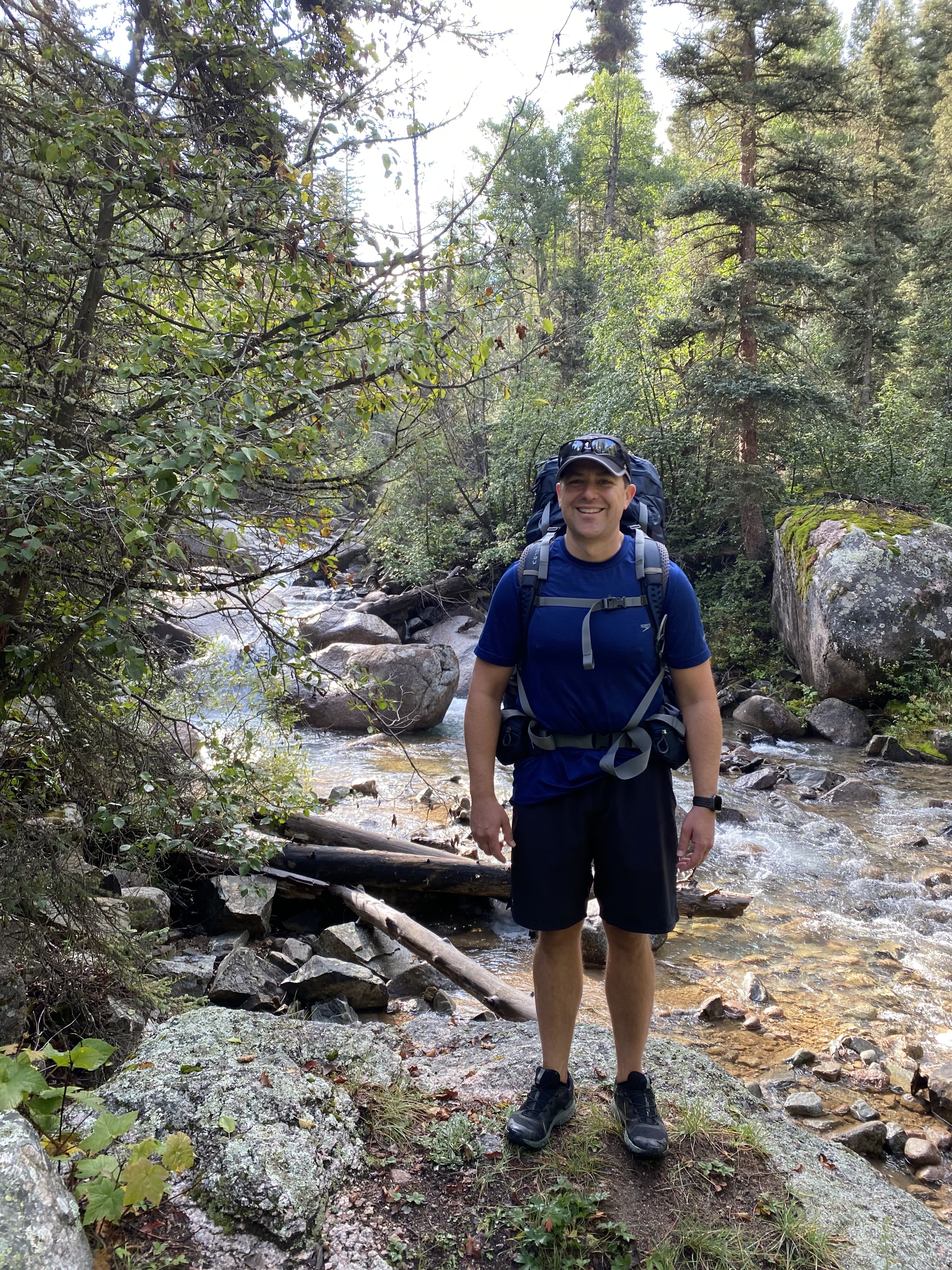 Tim Cook near river backpacking with trees in the background.